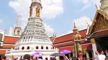 Wat Phra Kaew 'in Bangkok' taki manastırının dinamik görüntüsü, parlak gün ışığında hareketli ziyaretçilerle karışık mimarisini gözler önüne seriyor.