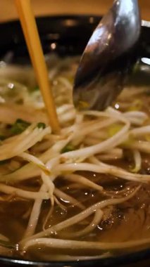 Sıcak ışık altında şehriye, biftek ve fasulye filizlerinin altını çizen, buharda pişmiş bir Vietnam flüt kasesinin yakın çekimleri.