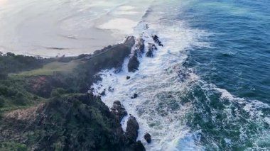 İnsansız hava aracı görüntüleri, Byron Körfezi 'nin engebeli sahil şeridini engebeli dalgalar ve verimli yeşilliklerle doğal gün ışığı altında yakalıyor.