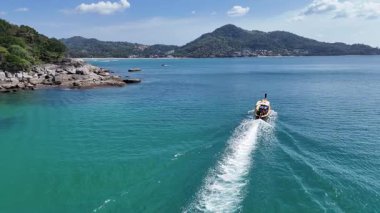 Phuket, Tayland yakınlarındaki berrak turkuaz sularda gün ışığında seyreden uzun kuyruklu bir teknenin hava görüntüsü.