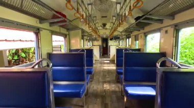 Mavi koltuklu boş bir trenin içinde, Kanchanaburi, Tayland 'da yemyeşil bir alanda ilerliyor. Doğal ışıklandırma ve sabit kamera.