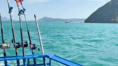 Chalong Körfezi, Phuket 'in turkuaz sularında bir teknede olta kamışı. Sakin deniz, berrak gökyüzü ve uzak adalar sakin bir atmosfer yaratır.