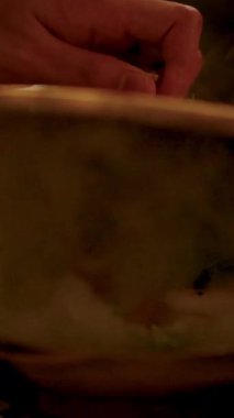 Bir el bir tencereyi açar, buharı tüten karides Miang Kham 'ı canlı malzemeler üzerine odaklanmış sıcak, altın bir ışıkta gösterir.