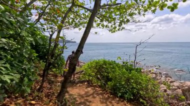 Phuket, Tayland 'da güpegündüz okyanus manzaralı gür bir kıyı şeridi boyunca yürüyen bir insan.