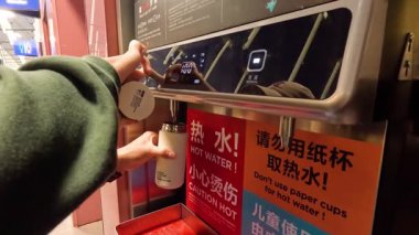 Sıcak su makinesinin bardağını dolduran kişi