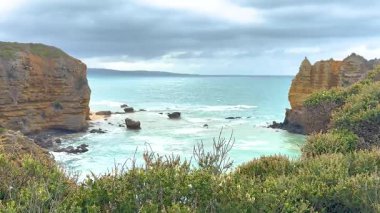 Büyük Okyanus Yolu, Avustralya 'da kayalıkları ve bulutlu gökyüzünün altındaki okyanus dalgalarıyla sakin bir kıyı manzarası.