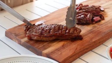 Biftek, iyi aydınlatılmış bir mutfakta, ahşap bir tahtanın üzerinde ustalıkla dilimlenir, dokuyu ve hassasiyeti ön plana çıkarır.