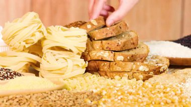 Bir el, tahıl ve ekmekleri sıcak ışıklandırma, doku ve çeşitliliği vurgulayan ahşap bir masa üzerinde organize eder.