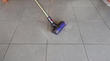 Elektrikli süpürge mutfak fayanslarındaki kırıntıları temizler. Parlak ışıklandırma temizlik sürecini ve döşeme dokusunu vurgular