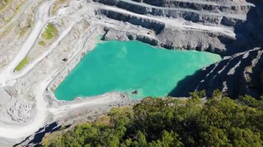 Parlak gün ışığı altında yemyeşil yeşilliklerle çevrili canlı turkuaz suyu olan teraslı bir taş ocağının hava görüntüleri.