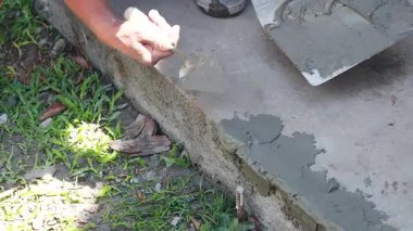 Bir işçi gün ışığında kaldırıma ıslak beton döker, ustalık ve detaylara dikkat gösterir.