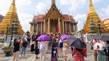 Turistler, güneşli bir günde tapınağın ihtişamını yakalamak için canlı şemsiyeler altında Bangkok, Tayland 'da Wat Phra Kaew' i keşfediyorlar.