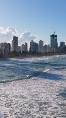 İnsansız hava aracı, açık gökyüzü altında altın rengi gökyüzü ve okyanus dalgalarını yakalıyor. Canlı gün ışığında kentsel ve doğal güzellikleri vurguluyor.