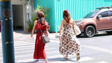 Phuket, Tayland 'da canlı elbiseli iki kadın karşıdan karşıya geçiyor. Parlak gün ışığı, kentsel ortam, dinamik çerçevelerde yakalanan günlük gezinti.