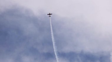Tek bir uçak dikey olarak yükselir, hava gösterisi sırasında bulutlu bir gökyüzüne karşı duman izi bırakır.