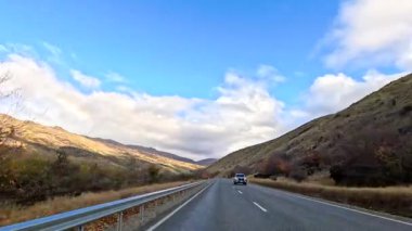 Wanaka 'nın pitoresk yollarında sakin bir sürüş, parlak mavi gökyüzünün altında canlı sonbahar yaprakları sergiliyor.