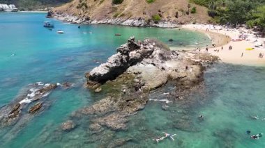 Hava görüntüleri Phuket, Tayland 'da kayalık oluşumlar, turkuaz sular ve güneşli günün tadını çıkaran kumsalcıları gösteren manzaralı bir sahili yakalar.