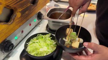 Bir şef, Bangkok restoranında Kore barbeküsü ve pırasa birleştiriyor. Ilık ışıklandırma yemek pişirme atmosferini arttırır.