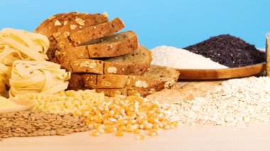 Tahta bir zemin üzerinde çeşitli tahıl, makarna ve ekmek sıralanmış parlak mavi bir zemin, dokusu ve rengi vurguluyor.