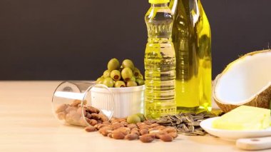 Parlak ışıklandırmalı ahşap bir masaya yerleştirilmiş yağlar, fındıklar ve avokadolar dahil çeşitli sağlıklı yağlar.