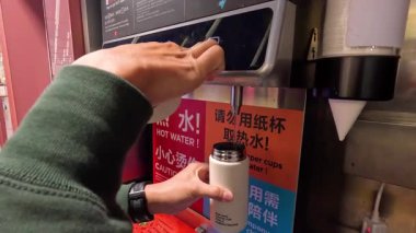 Kendi bardağıyla sıcak su dağıtıcısı kullanan kişi.