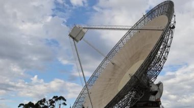 Bir radyo teleskobu bulutlu gökyüzünün altında döner.