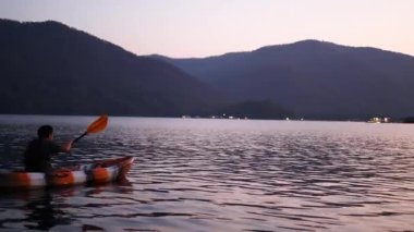 Gün batımında sakin bir gölde kano süren iki kişi.