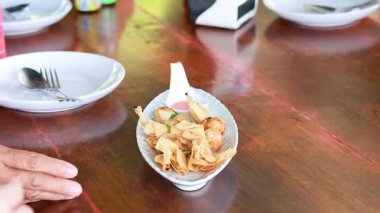 Tahta bir masanın üzerinde Tayland usulü para çantası köftesi servis eden biri, doğal ışıklandırmalı sıradan bir yemek takımını vurguluyor.