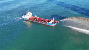 Parlak güneş ışığı altında temiz okyanus sularında kum pompalayan bir tarama gemisinin hava görüntüsü.