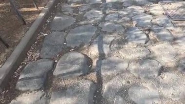 Bir kaldırım taşı yolunda yürüyen kişi, gölgeler bırakır.