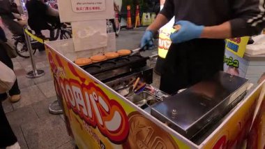 Tedarikçi işlek sokak tezgahında sosis ızgarası yapıyor.