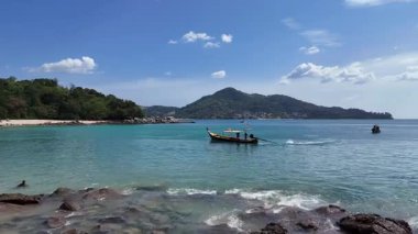 Uzun kuyruklu bir tekne Phuket, Tayland yakınlarındaki berrak turkuaz sularda dolaşır, dingin tropikal manzaralar ve canlı gökyüzü sergiler.