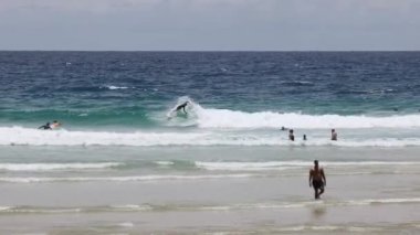 İnsanlar sahilde sörf ve yüzüyorlar.