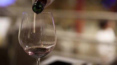 Bir bardağa dökülen kırmızı şarabın yakın çekim sekansı dökümün zarafetini ve hassasiyetini vurguluyor.
