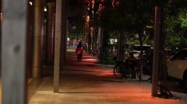 Geceleri ağaçlarla kaplı bir patikada yürüyen biri.