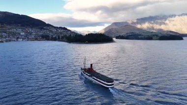 Bir buharlı gemi Wakatipu Gölü 'nde arka planda dağlık Queenstown ile yumuşak, doğal ışıklandırma altında yol alır.