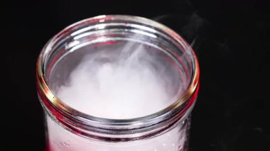 Kuru buzlu bir deney şişesi, kontrollü ışık altında büyüleyici bir kimyasal reaksiyon gösteren girdap oluşturur.