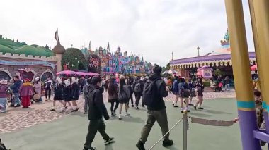 Ziyaretçiler bulutlu gökyüzünün altında Tokyo Disneyland 'da geziniyor, canlı atmosferi ve renkli çevreyi yakalıyorlar.