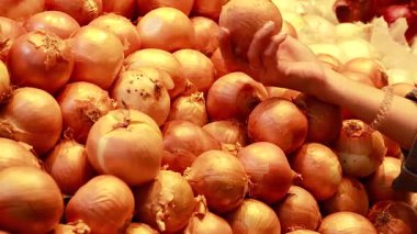 Bir insan sıcak ışık altında süpermarketteki sarı soğanları inceler ve seçer.