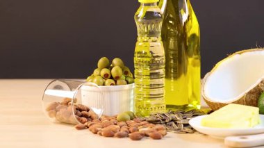 Yağlar, fındıklar ve avokadolar da dahil olmak üzere çeşitli sağlıklı yağlar parlak ışık altında ahşap bir yüzeye yerleştirilmiştir.