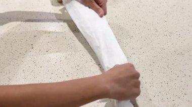 Eller ustalıkla yeniden kullanılabilir bir poşeti parlak ışıklandırma altında katlayarak verimli depolama teknikleri gösteriyor.