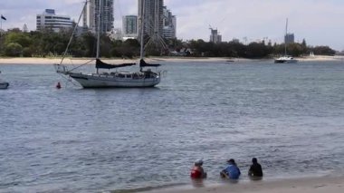Suyun kenarında oturup, tekneleri izleyen üç kişi.
