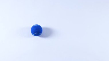 Mavi bir tenis topu yüzey boyunca yuvarlanıyor.