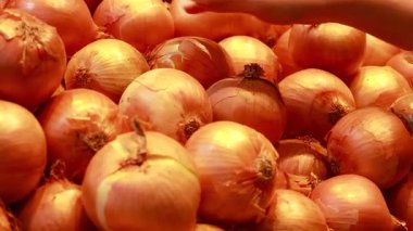 Eller canlı bir süpermarketten sarı soğan seçer. Ilık ışık altında, bir bakkal alışverişi anını yakalar.