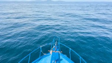 Phuket, Tayland yakınlarındaki sakin okyanus sularında berrak gökyüzü ve parlak güneş ışığı altında bir tekne sorunsuzca süzülür.