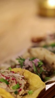Ahşap bir masanın üzerinde canlı malzemelerle, mum ışığıyla hafifçe aydınlatılmış, sıcak ve davetkar bir atmosfer yaratan tacoların yakın çekimi.