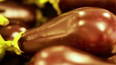 Canlı ışıklandırmalı taze patlıcanların yakın plan çekimleri bir pazar ortamında parlak dokularını vurguluyor.