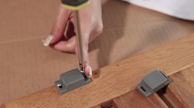 İyi ışıklandırılmış bir ortamda ahşap bir yüzeye mobilya monte etmek için tornavida kullanan ellerin yakın çekimi.