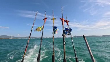 Tayland, Phuket 'te açık gökyüzünün altında hareket eden bir teknede sallanan oltalar. Canlı okyanus ve bayraklar dinamik bir sahne yaratır.