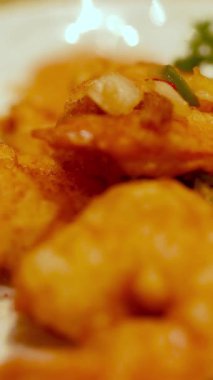 Sıcak ışık altında otlar ve sebzelerle süslenmiş gevrek karideslerin yakın çekimi.